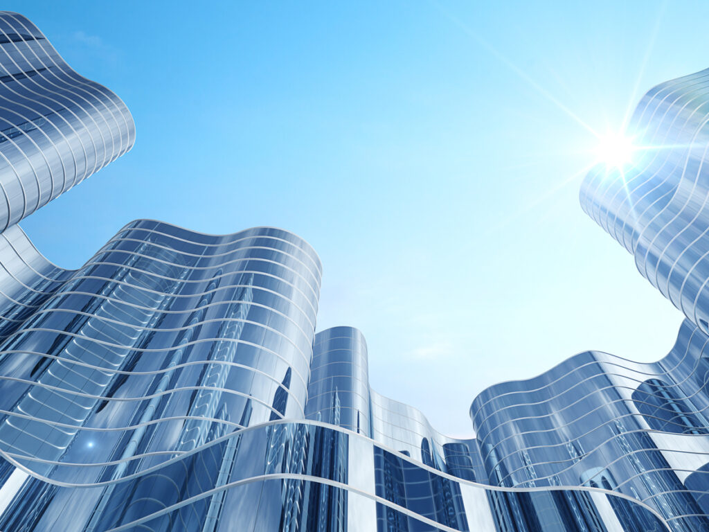 Modern curvilinear glass buildings under a clear blue sky with the sun shining brightly.