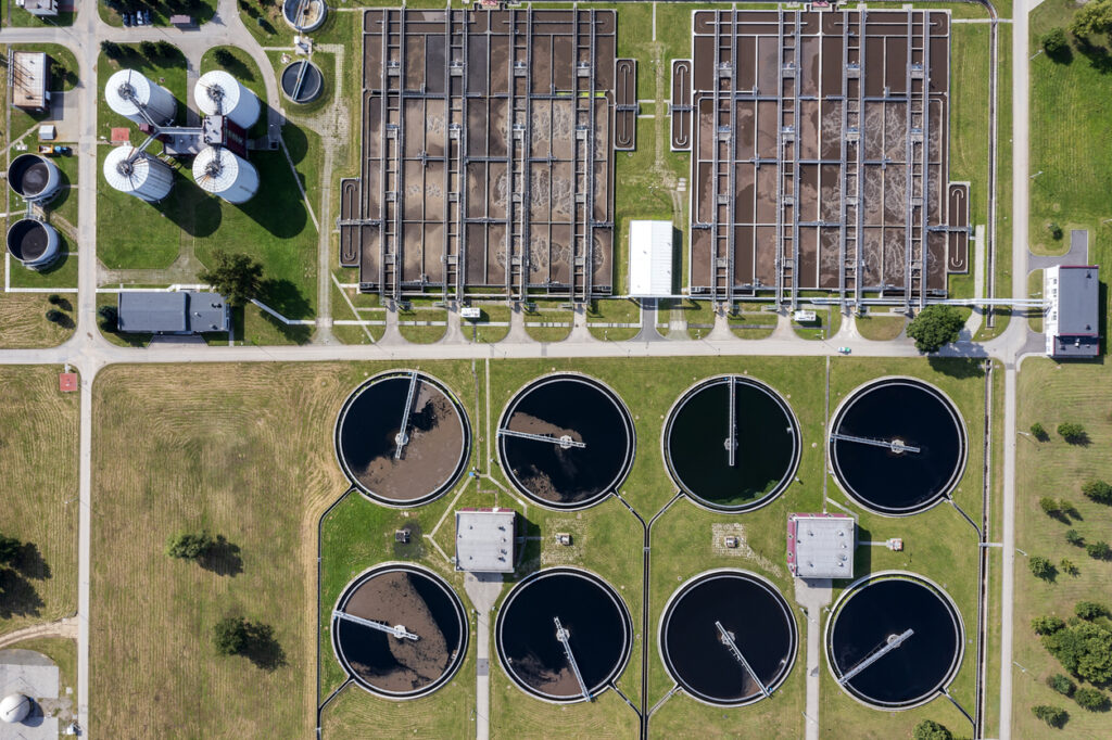 Aerial view of a wastewater treatment plant with circular settling tanks and rectangular aeration basins.