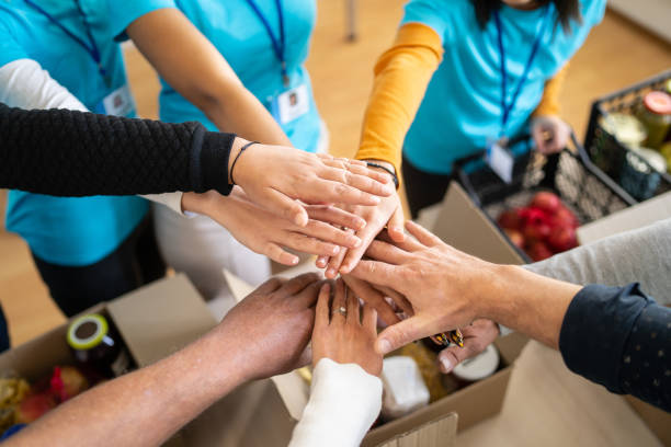 A group of people stacking hands over a box of food donations, symbolizing teamwork and community support.