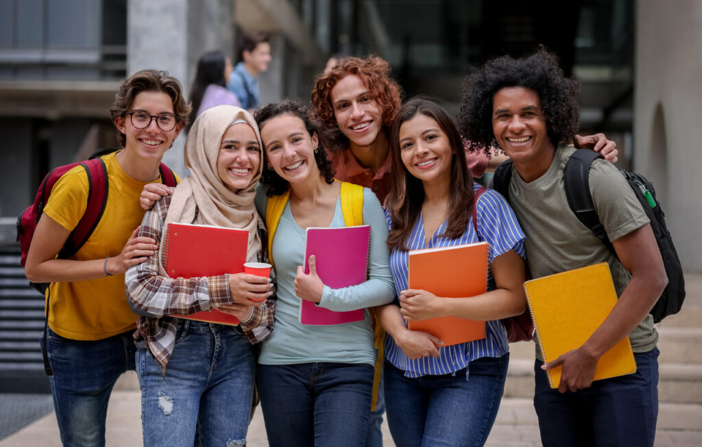 Diverse group of smiling students with backpacks and notebooks standing together on a campus.