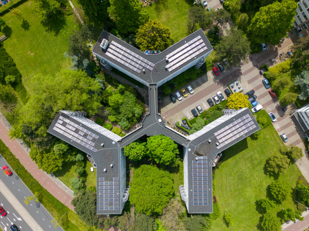 Aerial view of a y-shaped building with solar panels on the roof surrounded by greenery and parked cars.