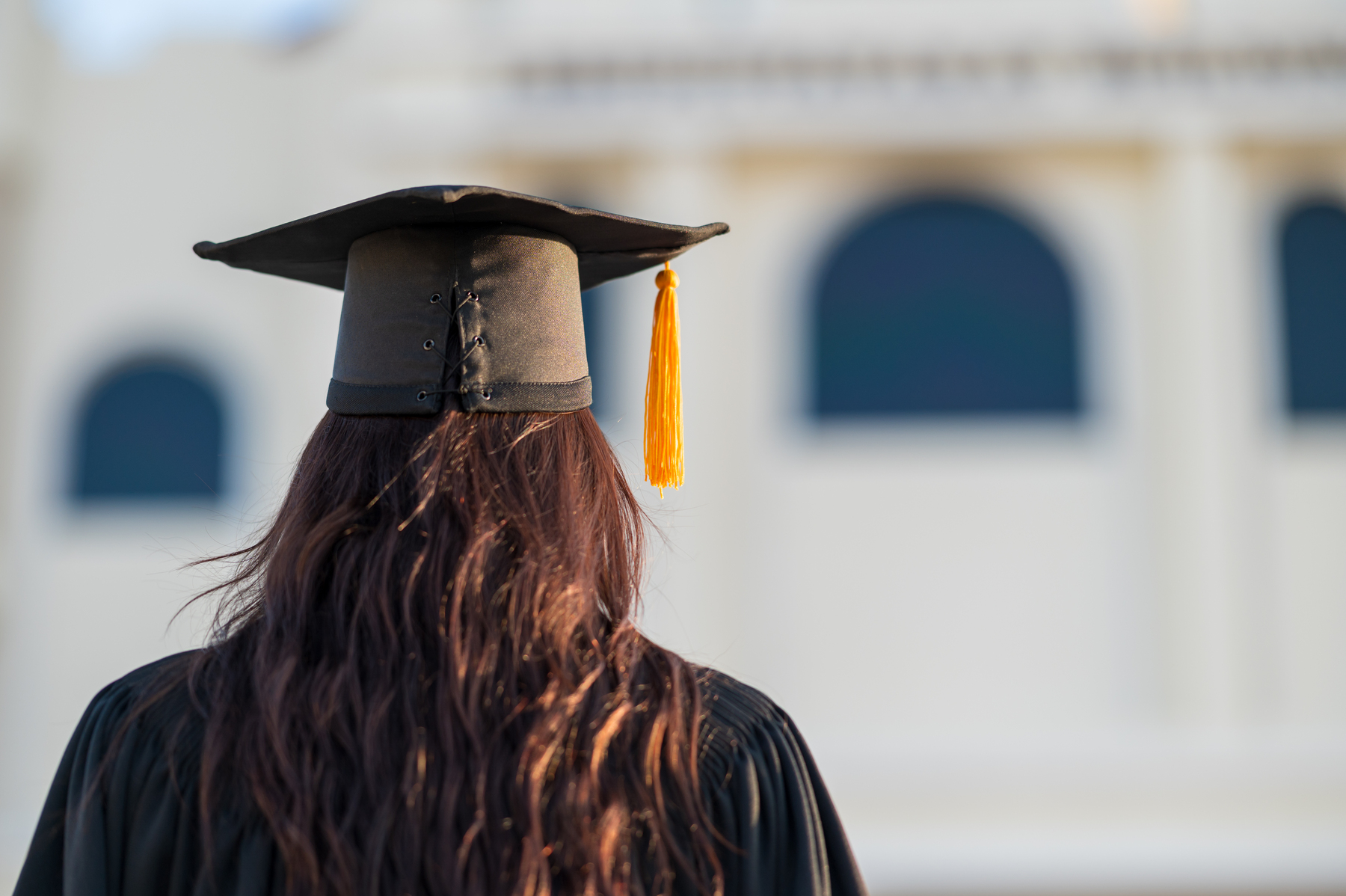 Graduate in cap and gown looking towards a building, symbolizing achievement and the next phase of life.