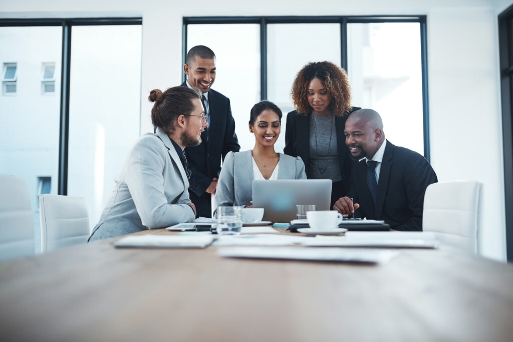 A diverse group of business professionals engaged in a discussion around a budget book and laptop at a conference table.