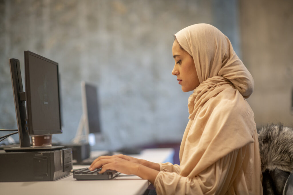 Woman in a hijab working at a computer desk.