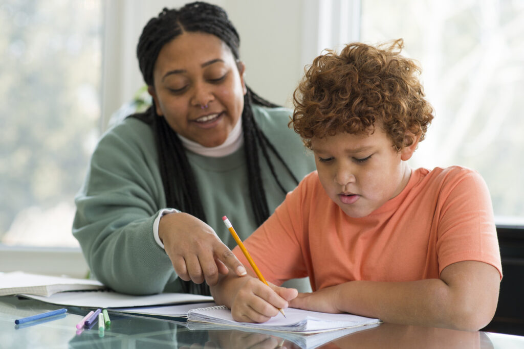 A woman helping a young boy with his homework at a table.