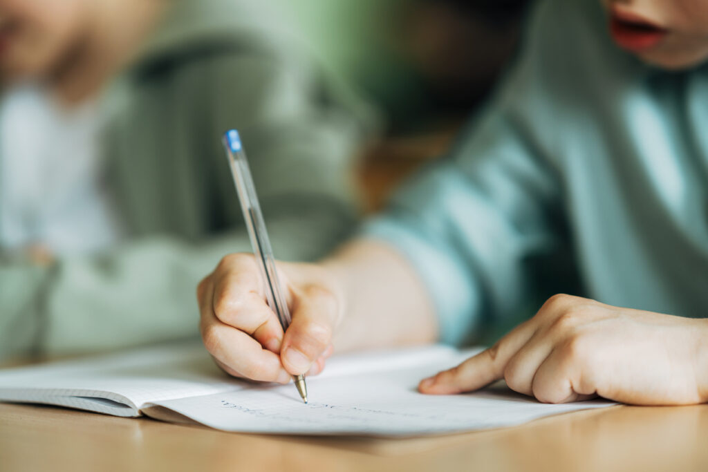 Child writing in a notebook with a pen.