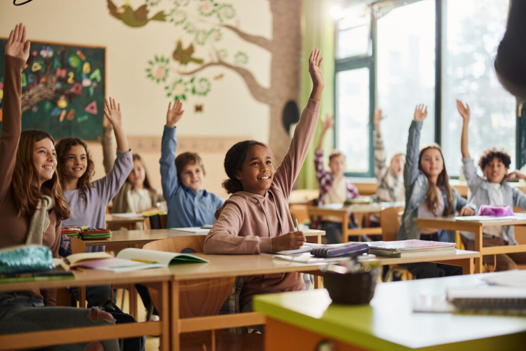 Students raising their hands eagerly in a classroom setting.